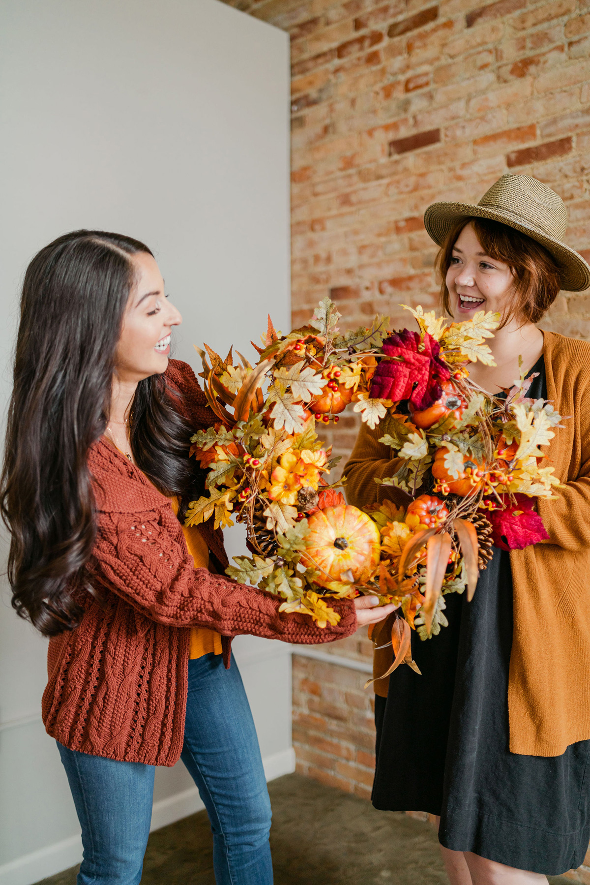 Two smiling women holding a fall wreath showing you how to style your porch for fall