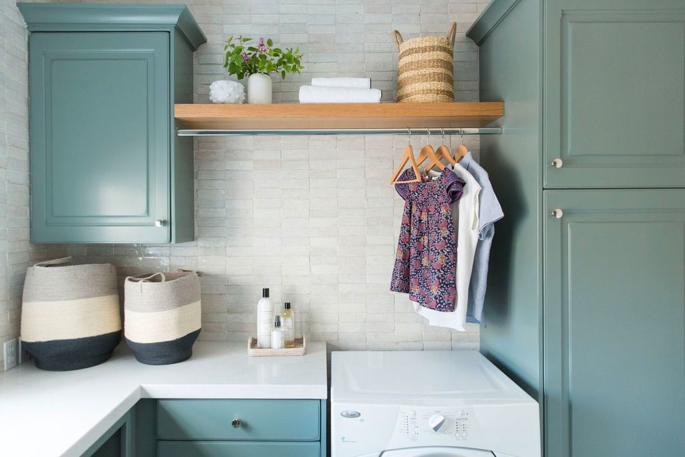 Small laundry room with teal cabinets and clothes hanging over the dryer.