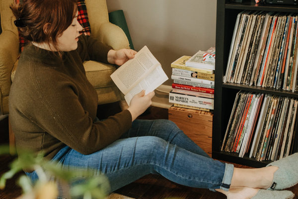 Woman sitting on the floor by a bookcase while reading a book.