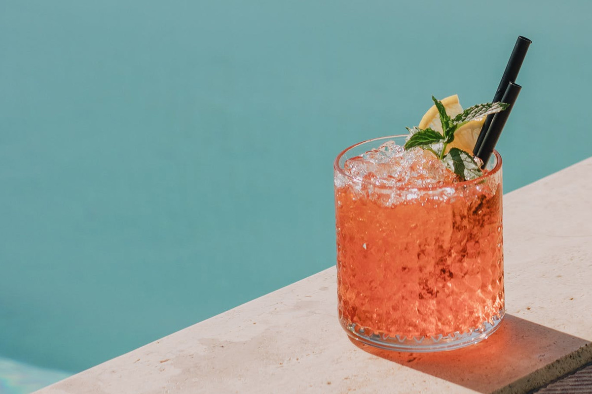 Poolside cocktail in a glass with two small straws and mint.